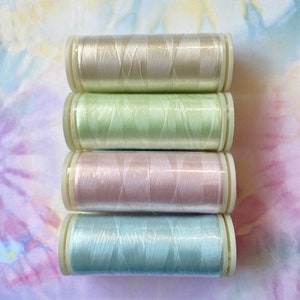 May include: Four spools of thread in pastel colors: cream, light green, pink, and light blue. The spools are stacked on top of each other.