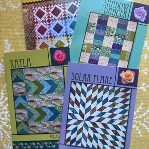 May include: Four quilting pattern cards with colorful quilt designs and the names "Square Box", "Shadow Dancer", "Kayla", and "Solar Flare". Each card features a different quilt pattern and the name of the pattern.