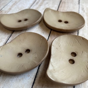 May include: Four brown, two-hole buttons with a textured surface. The buttons are shaped like a rounded rectangle.