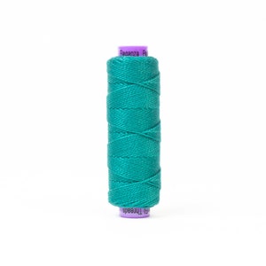 Puede incluir: Una bobina de hilo verde azulado con el texto "Eleganza Perla" y "Fil Threads" en la etiqueta.