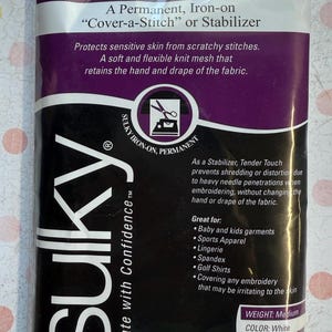 May include: A package of Sulky Tender Touch stabilizer. The package is white and purple with the Sulky logo and product information. The stabilizer is iron-on and measures 20" x 36". It is designed to protect sensitive skin and prevent distortion during embroidery.