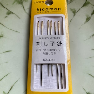 May include: A package of Hidamari Sashiko needles. The yellow and white package contains several needles with gold-colored eyes. The text on the package includes "Sashiko Needles" and Japanese characters. The package is marked "Made in Japan."