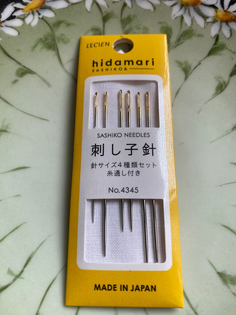 May include: A package of Hidamari Sashiko needles. The yellow and white package contains several needles with gold-colored eyes. The text on the package includes "Sashiko Needles" and Japanese characters. The package is marked "Made in Japan."