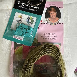 May include: A package of teal zipper slides by Pam Damour, with a variety of colors. Also, a package with 3 yards of olive zipper tape and 8 slides. The items are for sewing and crafting.