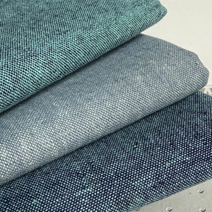 May include: Three folded layers of textured fabric stacked vertically. The top layer is a vibrant teal, the middle layer is a light heathered gray, and the bottom layer is a deep navy blue. Each piece of fabric features a visible woven pattern.