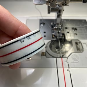 May include: A white tape measure with black and red lines. The tape measure is marked with 1/4 inch increments.