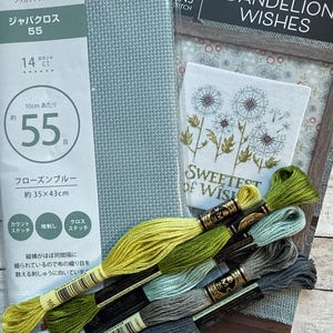 May include: A cross-stitch kit with a light blue fabric, embroidery floss in various shades of green and gray, and a pattern that says "Dandelion Wishes". The kit includes aida cloth, floss, and instructions for a counted cross-stitch project.