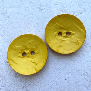 May include: Two large, round, yellow buttons with a textured surface. The buttons have two holes each.