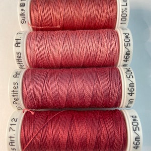 May include: Four spools of red thread, each with a white label. The labels have the text "Hes Art. 712 Petites Art. 7", "Petites Art. 7", "Sulky @ 12", and "46m/50yd 46m/50yd/ 100% Long".
