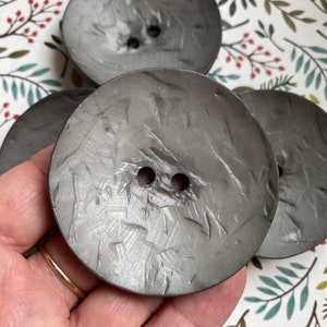 May include: Three silver-colored buttons with a textured surface. The buttons have two holes each.