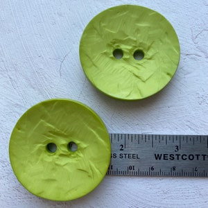 May include: Two lime green plastic buttons with a textured surface. The buttons are approximately 1 inch in diameter.
