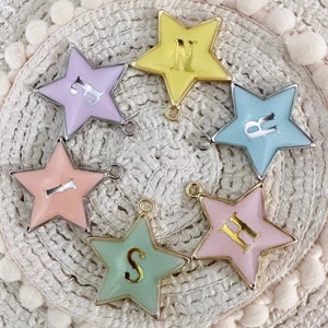 May include: A selection of star-shaped charms in various pastel colours. Each charm has a silver border and a letter in the centre. The charms are designed with a small loop for attaching to jewellery or other crafts.