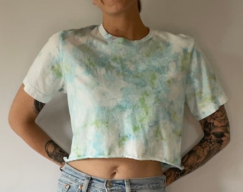 May include: A light blue tie-dye cropped t-shirt with a white background and green accents.