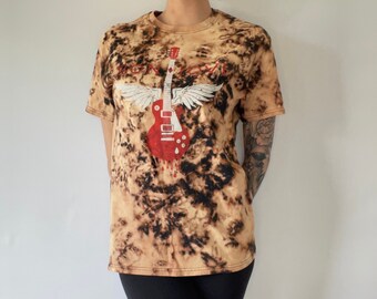 May include: A tie-dye t-shirt with a black and brown pattern. The shirt features a red electric guitar with wings and a blood drip effect. The text "Rock N Roll" is printed on the shirt.