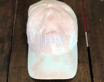 May include: A pink and white tie-dye baseball cap with the word "LEVI'S" embroidered in white on the front.
