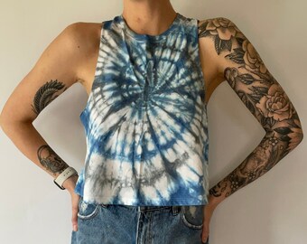May include: A blue and white tie-dye cropped tank top with a spiral pattern. The tank top is worn with denim shorts.