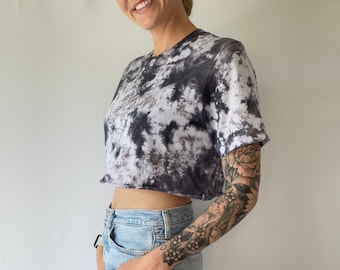 May include: A cropped tie-dye t-shirt in black and white with a short sleeve. The shirt is worn with light blue jeans.