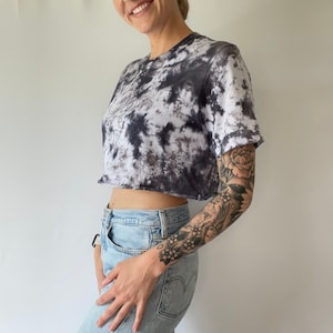 May include: A cropped tie-dye t-shirt in black and white with a short sleeve. The shirt is worn with light blue jeans.