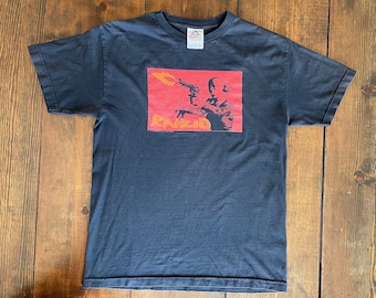 May include: Black t-shirt with a red and orange graphic of a person holding a gun. The graphic says "Rancid" in orange letters.