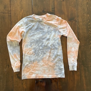 May include: A long-sleeved shirt with a tie-dye pattern in shades of peach, gray, and white.
