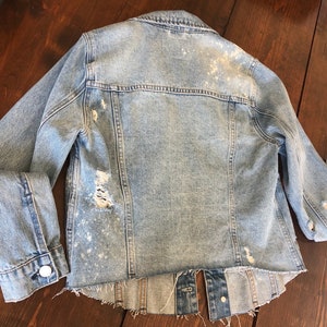 May include: Light blue denim jacket with distressed details and a frayed hem.