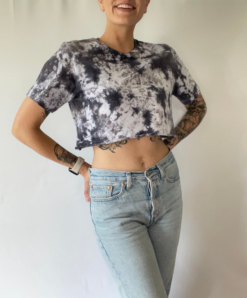 May include: A black and white tie-dye cropped t-shirt with a relaxed fit. The shirt has a raw edge hem and is made of a soft, comfortable fabric.