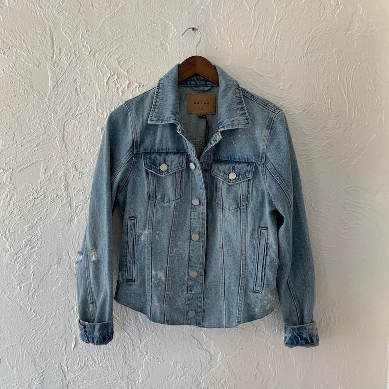 May include: Light blue denim jacket with a distressed look and a faded wash. The jacket has a button closure, two chest pockets, and two front pockets.