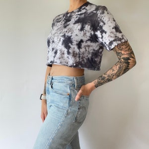 May include: A cropped tie-dye t-shirt in black and white with a relaxed fit. The shirt is made of a soft, comfortable fabric and has a crew neckline.