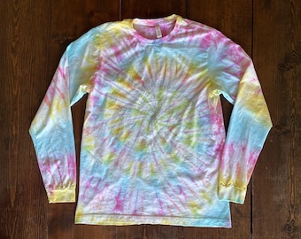 May include: A long-sleeved shirt with a tie-dye pattern in shades of pink, yellow, and blue. The shirt has a circular pattern with a swirl design.