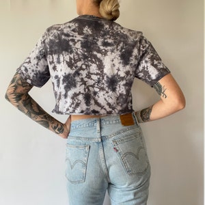 May include: A black and white tie-dye cropped t-shirt with light blue denim jeans.