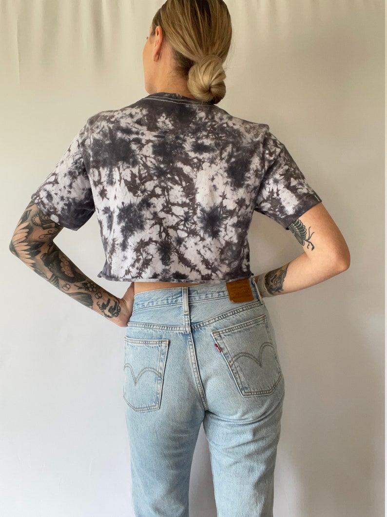 May include: A black and white tie-dye cropped t-shirt with light blue denim jeans.