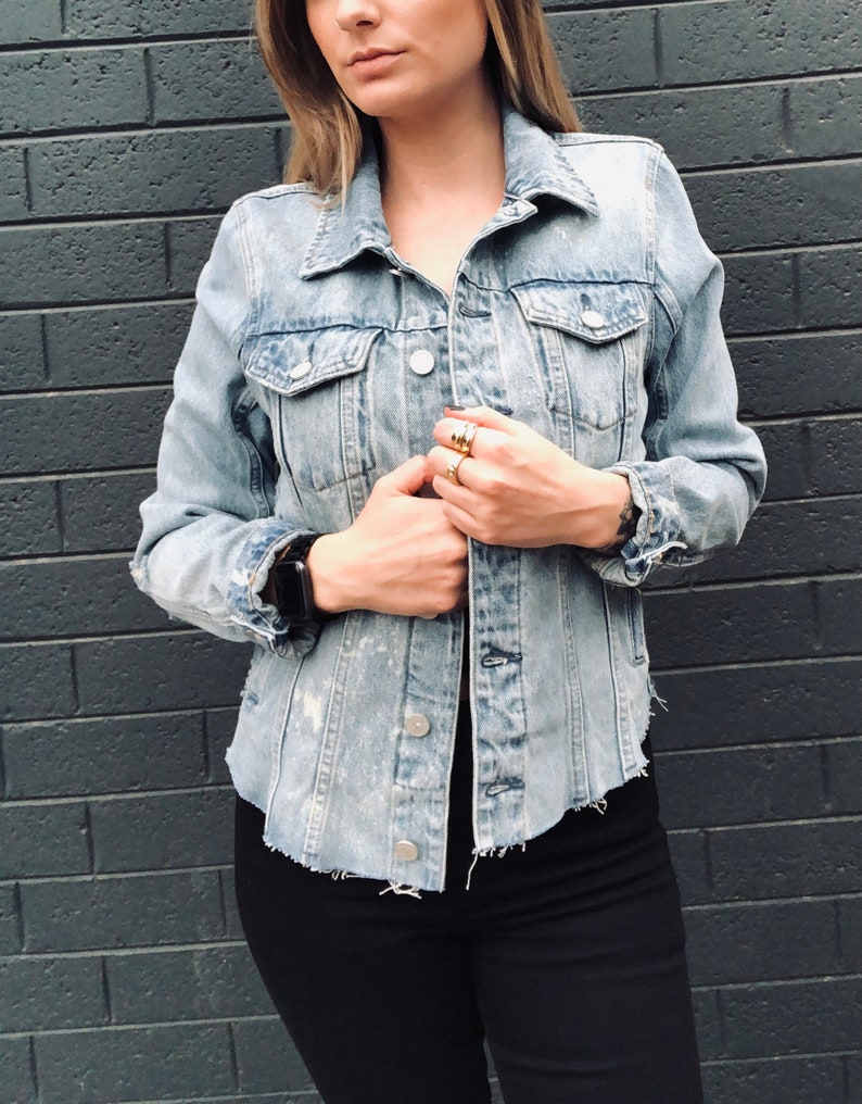 May include: A light blue denim jacket with frayed edges and a distressed look. The jacket has a button closure and multiple pockets.