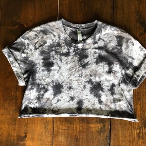 May include: A gray and white tie-dye cropped t-shirt with short sleeves. The shirt has a relaxed fit and a slightly rolled cuff.