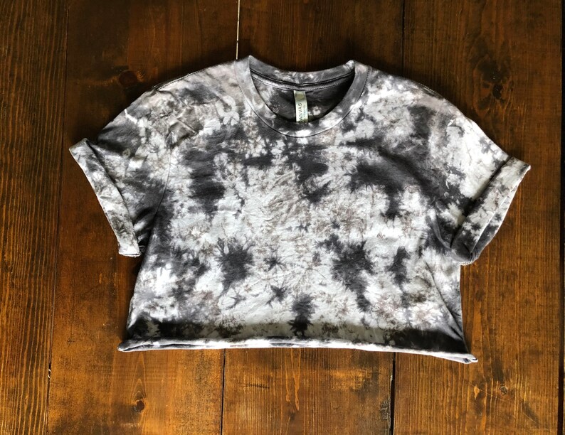 May include: A gray and white tie-dye cropped t-shirt with short sleeves. The shirt has a relaxed fit and a slightly rolled cuff.