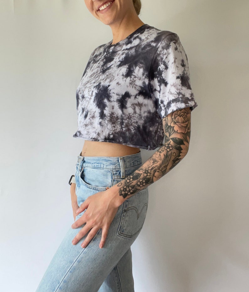 May include: A cropped tie-dye t-shirt in black and white with a short sleeve. The shirt is worn with light blue jeans.