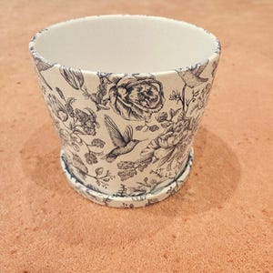 May include: White ceramic planter with a black and white floral pattern featuring hummingbirds and roses.