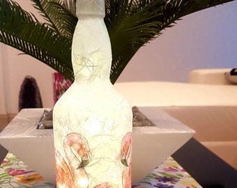 Puede incluir: Una botella de vidrio blanco con un tapón de corcho y una luz en el interior. La botella está decorada con un diseño de flamencos rosas.