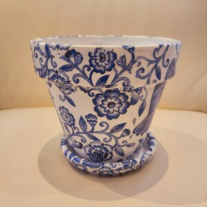 May include: A white ceramic flower pot with a blue and white floral pattern. The pot has a matching saucer.