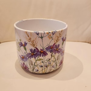May include: White ceramic planter with a floral pattern featuring purple and yellow wildflowers.
