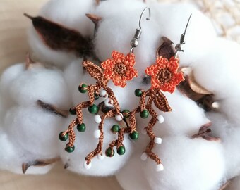 May include: A pair of crocheted earrings with orange flowers, green beads, and white beads hanging from brown crocheted branches.