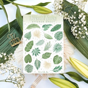 May include: A sticker sheet with a white background and a variety of green tropical leaves. The sheet is titled "Tropical Leaves Sticker Sheet" and has the text "Out of the Pen" at the bottom.