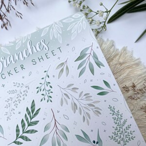 Op de afbeelding: Een stickerblad met een groene en witte gradi&euml;nt achtergrond met verschillende groene en witte takken en bladeren. De tekst "Branches Sticker Sheet" staat in cursief bovenaan het blad.