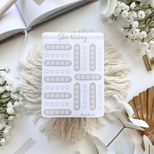 May include: A sheet of white planner stickers with a light brown background. The stickers feature various star ratings from one to five stars. The text "Star Rating Planner Stickers" is at the top of the sheet. The text "Out of the Box" is at the bottom of the sheet.