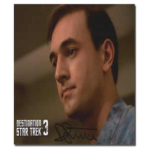 May include: A close-up of a man's face with a serious expression. He is wearing a blue and white patterned shirt. The image is signed "DeForest" and includes the text "Destination Star Trek 3".
