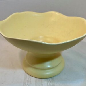 May include: A pale yellow ceramic pedestal bowl with a scalloped rim. The bowl is on a white background.