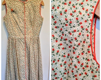 May include: A sleeveless dress with a floral print featuring red and white flowers on a beige background. The dress has a button-up front and a red trim around the neckline and armholes.