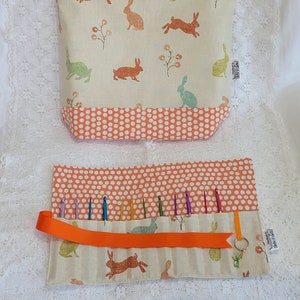 May include: A set of two fabric storage bags with a bunny and floral print. The larger bag has a drawstring closure and the smaller bag has a roll-up design with a ribbon closure and a key ring. Both bags have a polka dot pattern on the top and bottom.