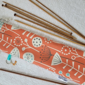 Peut inclure: Un jeu d'aiguilles à tricoter en bois dans un étui en tissu à motif floral. L'étui est orange avec des fleurs blanches et grises et une doublure à pois bleus et blancs. L'étui est doté d'une fermeture à cordon et d'une petite étiquette indiquant "Sewn with Sew".