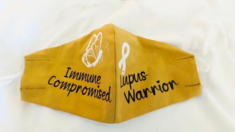 May include: A yellow face mask with a white butterfly and the text "Immune Compromised" on one side and a white ribbon with the text "Lupus Warrior" on the other side.
