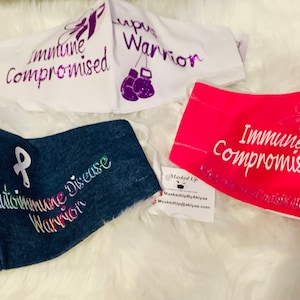 May include: Four fabric face masks with different designs and messages. The masks are white, denim, pink, and white. The messages on the masks include "Immune Compromised", "Cancer Warrior", "Autoimmune Disease Warrior", and "Immune Compromised".